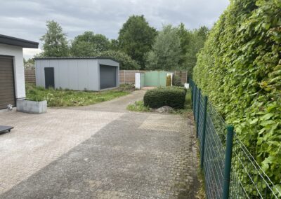 Een oprit in Hoboken met een groene haag en een garage.